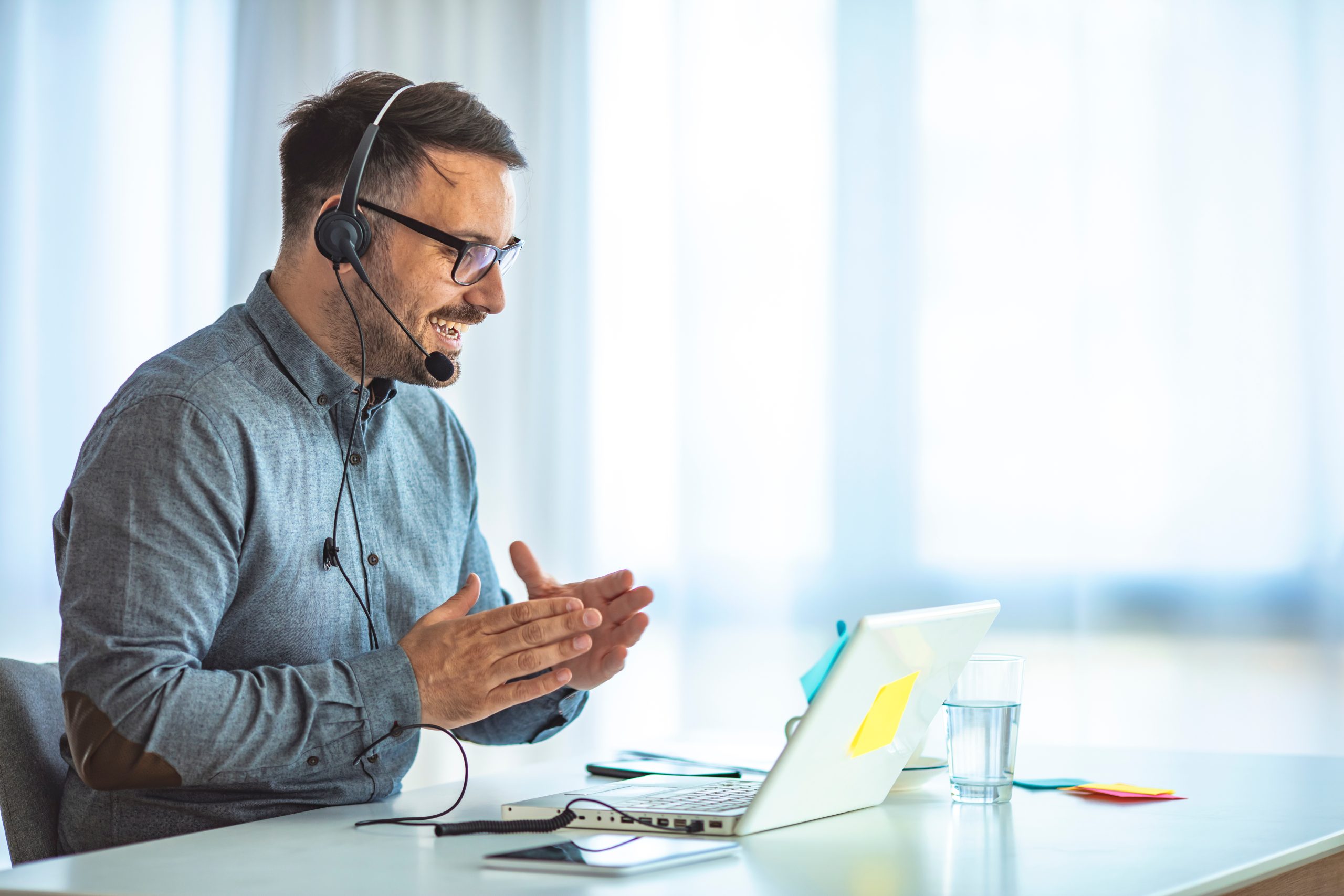 focused young businessman in eyewear wearing headphones, holding video call with clients on laptop. concentrated millennial man in glasses giving online educational class lecture, consulting customer.